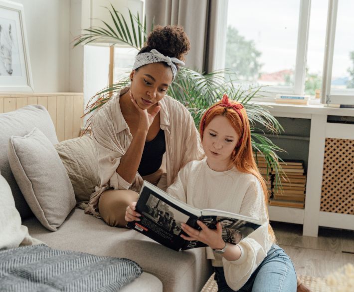 Two women sitting on a sofa reading a magazine together, symbolizing connection and friendship through Gofrendly.
